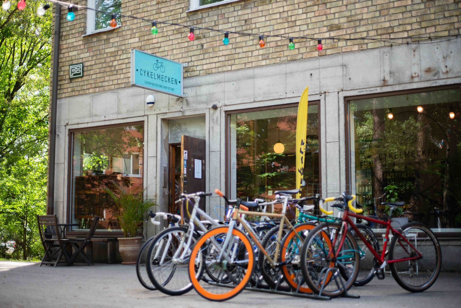 Cykelmeckens fasad på Blommensbergsvägen 178 med den turkosa skylten ovanför entrén, ljusslingor och en rad cyklar parkerade utanför